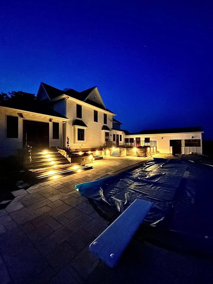 Twilight view of a modern home with a pool and illuminated backyard features.